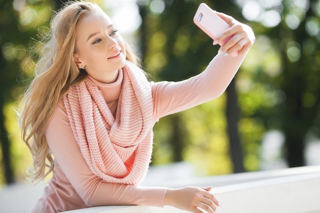Giovane donna attraente che rende selfie all'aperto. Ragazza casuale che parla sul telefono cellulare nel parco. Giovane signora attraente che chiacchiera con i suoi amici dal cellulare.