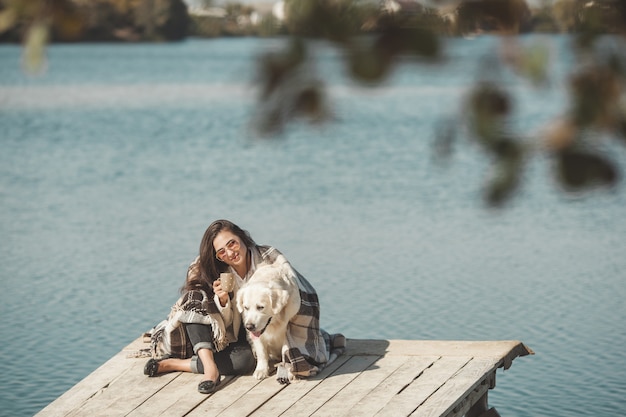 Giovane donna attraente che si siede al molo con il suo cane. Migliori amiche all'aperto