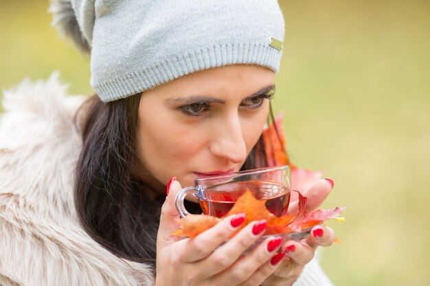 Giovane donna attraente che tiene in mano tè rosso caldo. Rilassarsi nella natura autunnale con tè caldo.