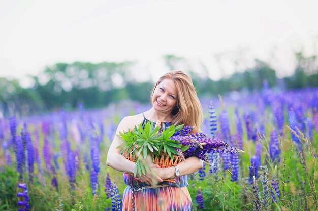 Giovane donna attraente che tiene un cesto pieno di fiori di lupino