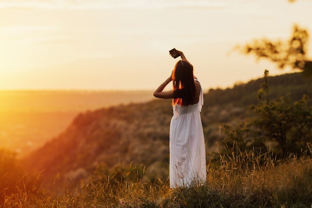 Giovane donna attraente che tiene uno smartphone e prendendo un selfie sulla collina