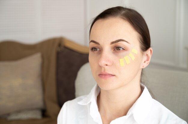 Giovane donna attraente con i capelli lunghi con kinesiotape giallo sul viso. Concetto di cosmetologia non invasivo.