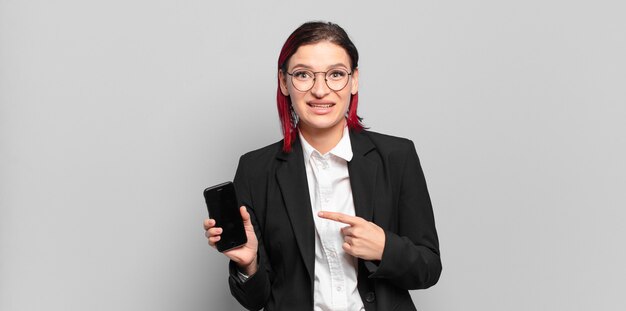 Giovane donna attraente con i capelli rossi che sorride allegramente, si sente felice e punta di lato e verso l'alto, mostrando l'oggetto nello spazio della copia. concetto di affari