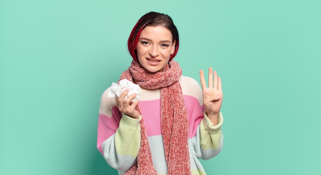 Giovane donna attraente dai capelli rossi che sorride e sembra amichevole, mostrando il numero quattro o il quarto con la mano in avanti, contando il concetto di influenza