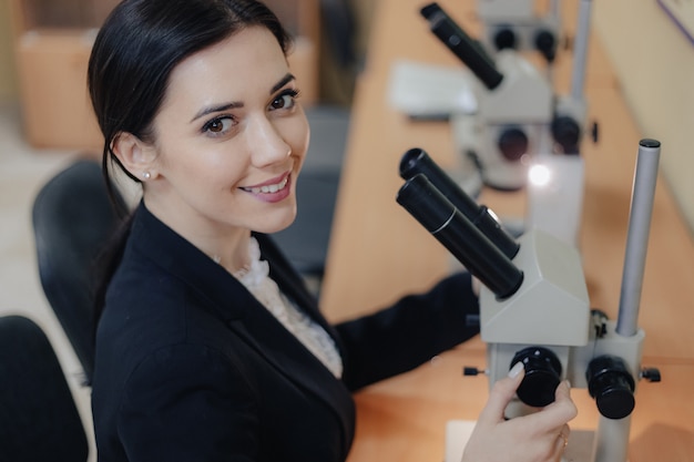 Giovane donna attraente emotiva che si siede al tavolo e lavora con un microscopio