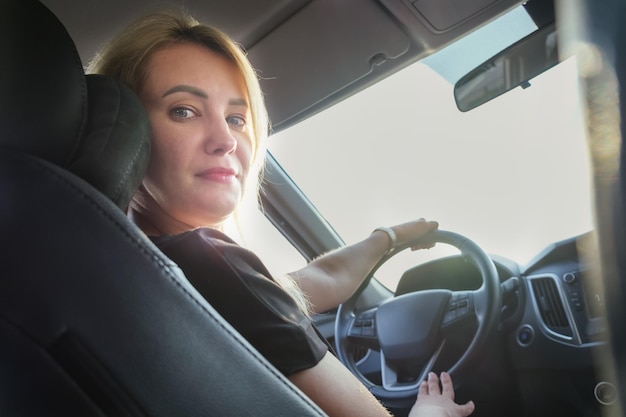 Giovane donna attraente guida un'auto Bella donna bionda con i capelli lunghi in un'auto durante la guida