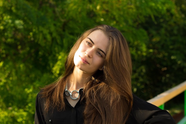 Giovane donna attraente in camicetta nera e collana d'argento sullo sfondo di alberi verdi