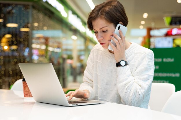 Giovane donna attraente seduta in un centro commerciale a un tavolo e lavorando a un computer portatile