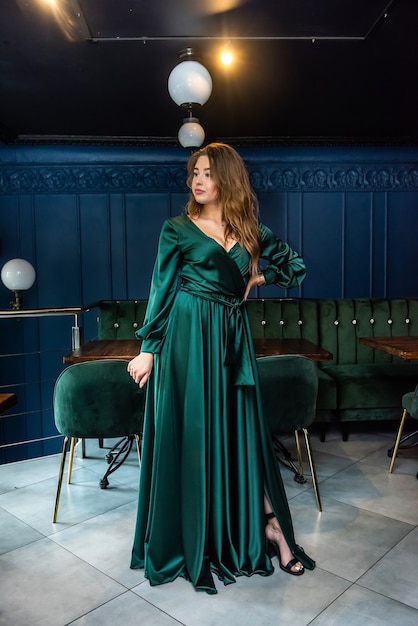 Giovane donna attraente sexy che porta vestito lungo verde che posa sulla sedia al caffè della città. eleganza