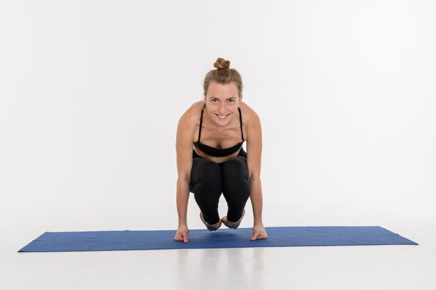 Giovane donna attraente sportiva che fa pratica di yoga su fondo bianco. Corvo - Bakasana.