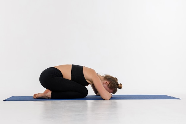 Giovane donna attraente sportiva che fa pratica di yoga su fondo bianco. Posa del bambino, Balasana.