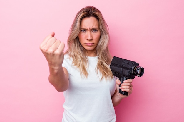 Giovane donna australiana che filma con una videocamera vintage isolata che mostra il pugno alla telecamera, espressione facciale aggressiva.