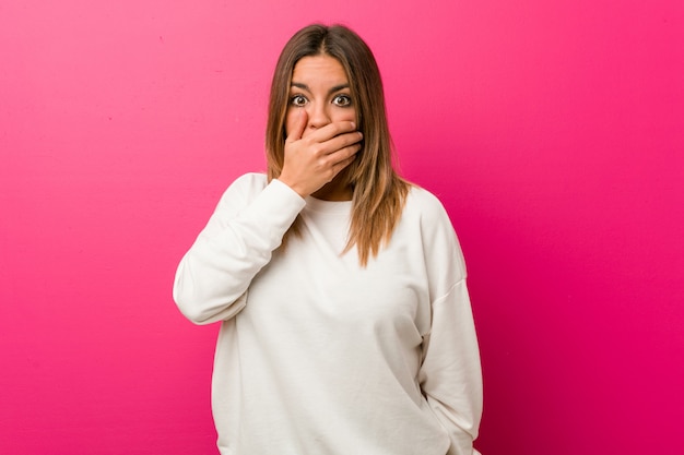 Giovane donna autentica carismatica vera gente contro un muro pensieroso guardando a uno spazio di copia che copre la bocca con la mano.