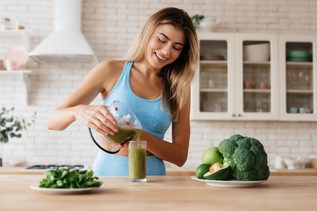 Giovane donna beata che sorride mentre purga un delizioso frullato verde in un bicchiere