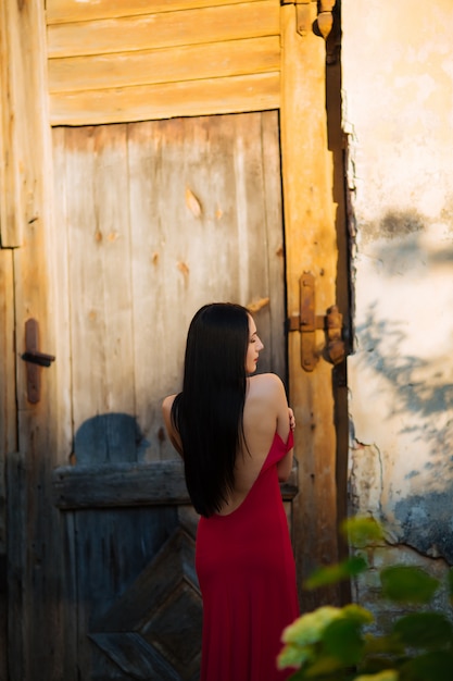 Giovane donna bellissima e molto elegante in un lungo abito da sera nero in posa su un muro grigio e porta, giornata di sole,