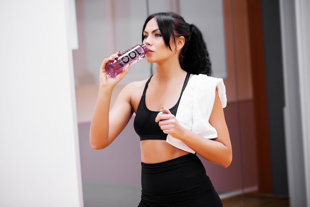 Giovane donna bere acqua pulita in palestra.