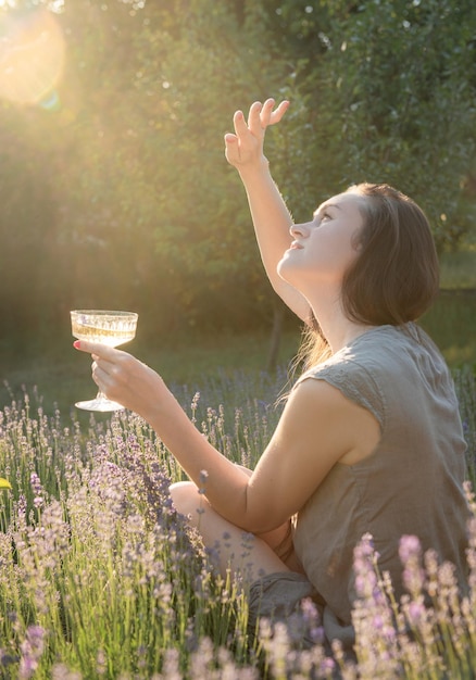 Giovane donna bere vino nel campo di lavanda al tramonto