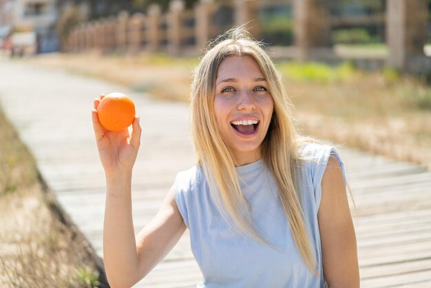 Giovane donna bionda all'aperto che tiene un'arancia