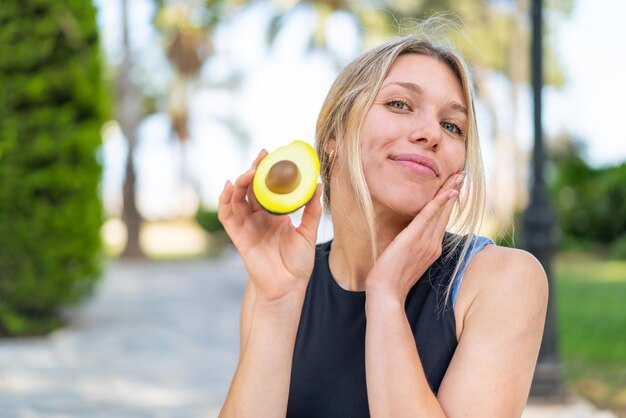 Giovane donna bionda all'aperto che tiene un avocado