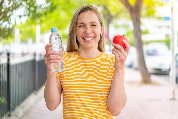 Giovane donna bionda all'aperto con una mela e una bottiglia d'acqua