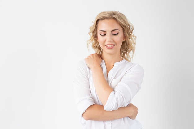 Giovane donna bionda allegra con capelli ricci lunghi che posano su una priorità bassa bianca con lo spazio della copia. Il