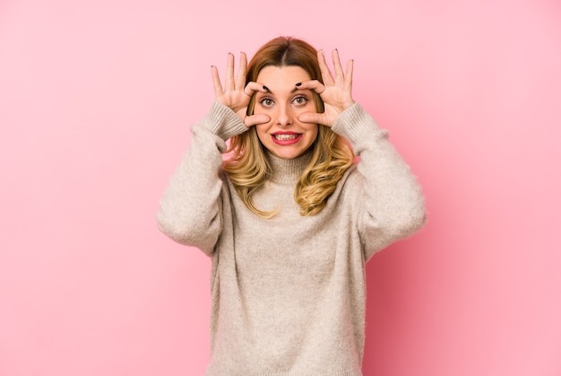 Giovane donna bionda carina che indossa un maglione isolato tenendo gli occhi aperti per trovare un'opportunità di successo.