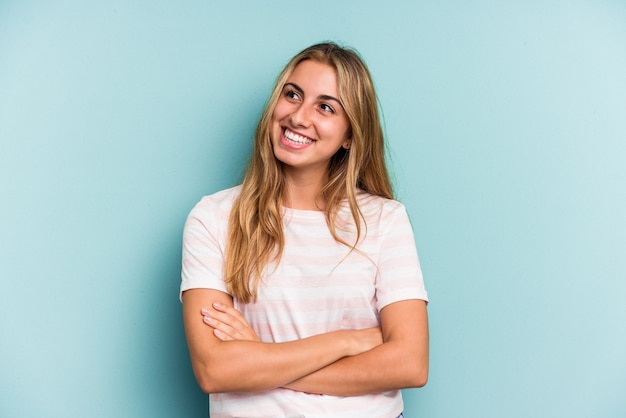 Giovane donna bionda caucasica isolata su sfondo blu sorridente fiducioso con le braccia incrociate.