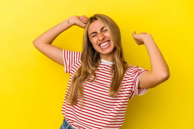 Giovane donna bionda caucasica isolata su sfondo giallo che celebra un giorno speciale, salta e alza le braccia con energia.