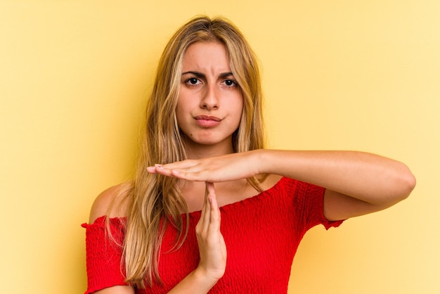 Giovane donna bionda caucasica isolata su sfondo giallo che mostra un gesto di timeout.