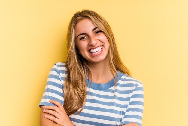 Giovane donna bionda caucasica isolata su sfondo giallo che si sente sicura, incrociando le braccia con determinazione.