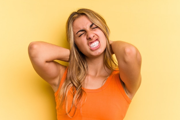 Giovane donna bionda caucasica isolata su sfondo giallo che soffre di dolore al collo a causa dello stile di vita sedentario.