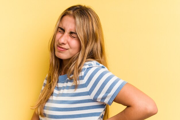 Giovane donna bionda caucasica isolata su sfondo giallo che soffre di mal di schiena.