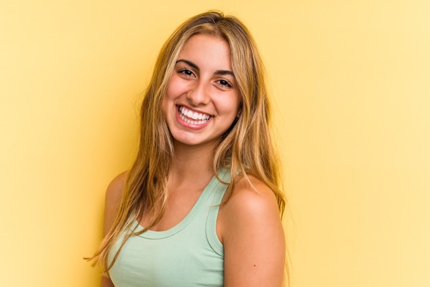 Giovane donna bionda caucasica isolata su sfondo giallo fiducioso tenendo le mani sui fianchi.