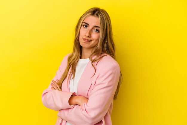 Giovane donna bionda caucasica isolata su sfondo giallo infelice guardando a porte chiuse con espressione sarcastica.