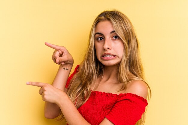 Giovane donna bionda caucasica isolata su sfondo giallo scioccata indicando con il dito indice uno spazio di copia.