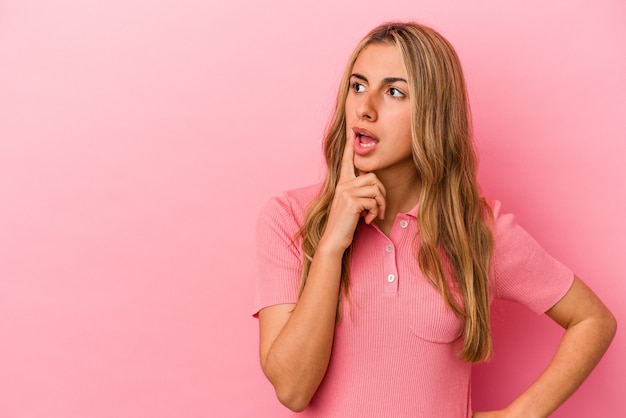 Giovane donna bionda caucasica isolata sulla parete rosa che guarda lateralmente con espressione dubbiosa e scettica