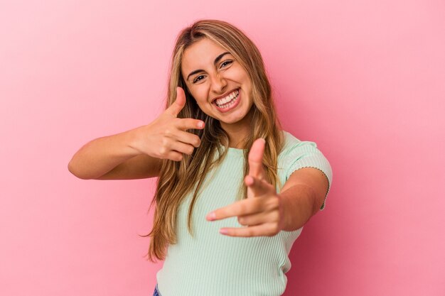 Giovane donna bionda caucasica isolata sulla parete rosa che punta in avanti con le dita