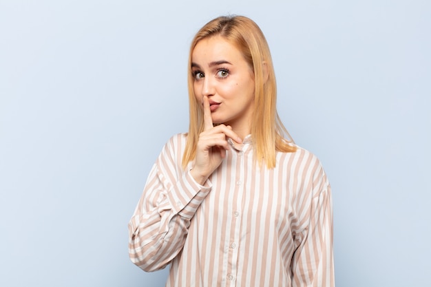 Giovane donna bionda che chiede silenzio e silenzio, gesticolando con il dito davanti alla bocca, dicendo shh o mantenendo un segreto