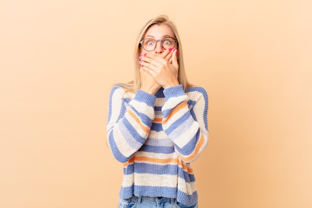 Giovane donna bionda che copre la bocca con le mani con uno shock