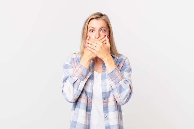 Giovane donna bionda che copre la bocca con le mani con uno shock