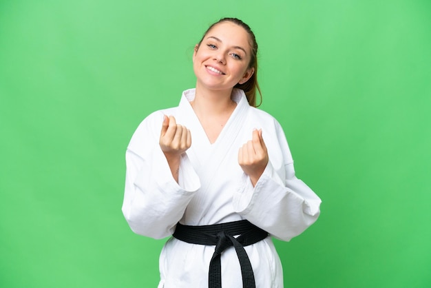 Giovane donna bionda che fa karate su sfondo chroma key isolato che fa gesto di denaro