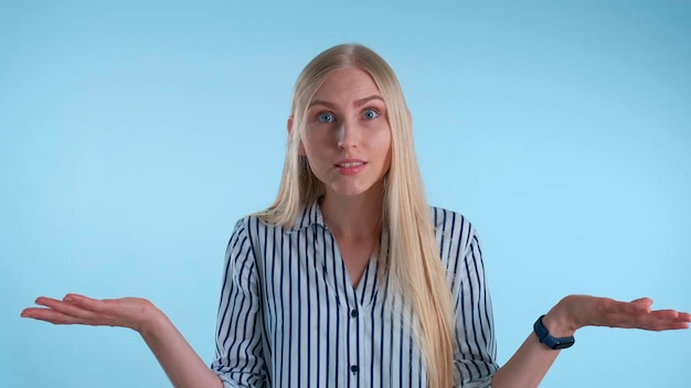 Giovane donna bionda che fraintende qualcosa su sfondo blu che mostra questa emozione sul viso e...