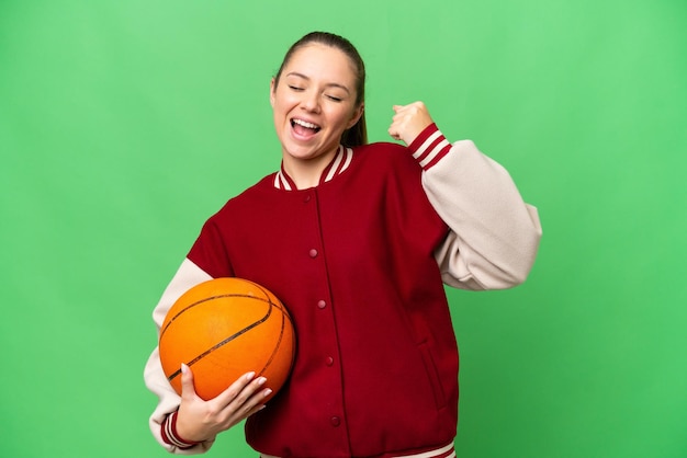 Giovane donna bionda che gioca a basket su sfondo chroma key isolato che celebra una vittoria