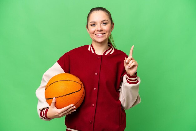 Giovane donna bionda che gioca a basket su sfondo chroma key isolato che punta su una grande idea