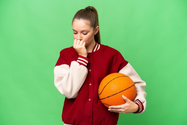 Giovane donna bionda che gioca a basket su sfondo chroma key isolato con dubbi