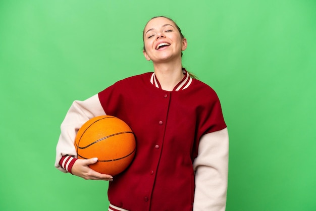 Giovane donna bionda che gioca a basket su sfondo chroma key isolato ridendo