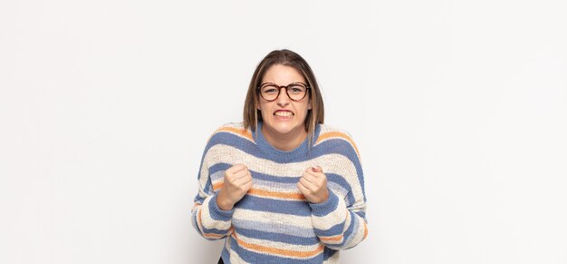 Giovane donna bionda che grida in modo aggressivo con sguardo infastidito, frustrato, arrabbiato e pugni stretti, sentendosi furioso