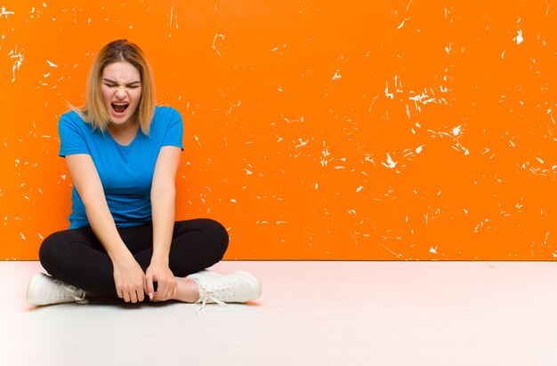 Giovane donna bionda che grida in modo aggressivo, sembra molto arrabbiata, frustrata, oltraggiata o infastidita, urlando di non sedersi sul pavimento