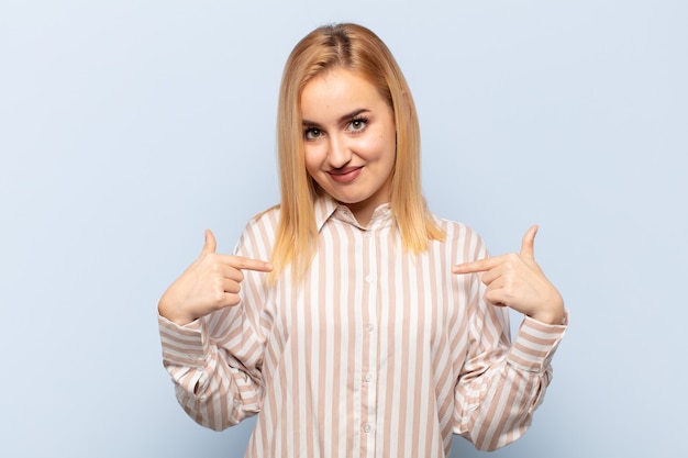 Giovane donna bionda che guarda orgoglioso, positivo e casual che punta al petto con entrambe le mani