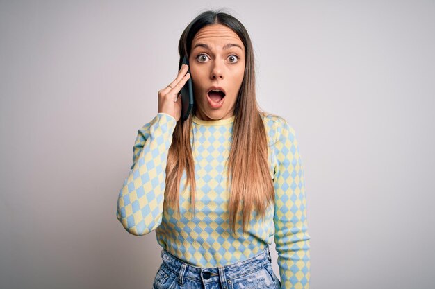 Giovane donna bionda che ha una conversazione che parla su smartphone su sfondo isolato spaventata in stato di shock con una faccia a sorpresa impaurita ed eccitata con espressione di paura